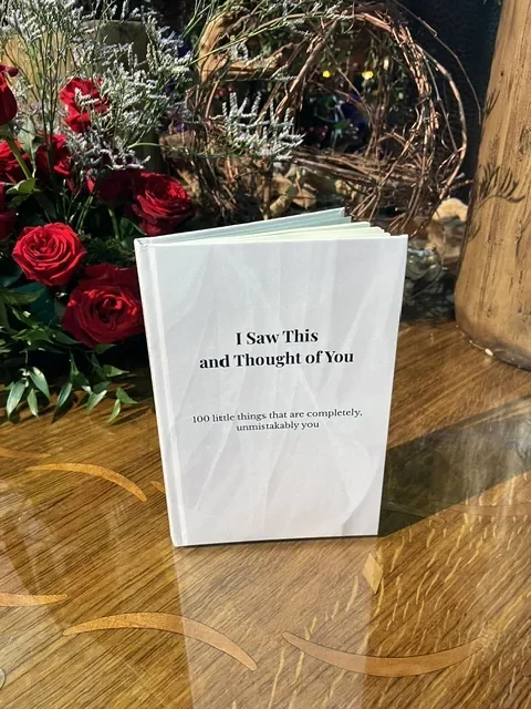I Saw This and Thought of You book standing on a wood table beside red roses